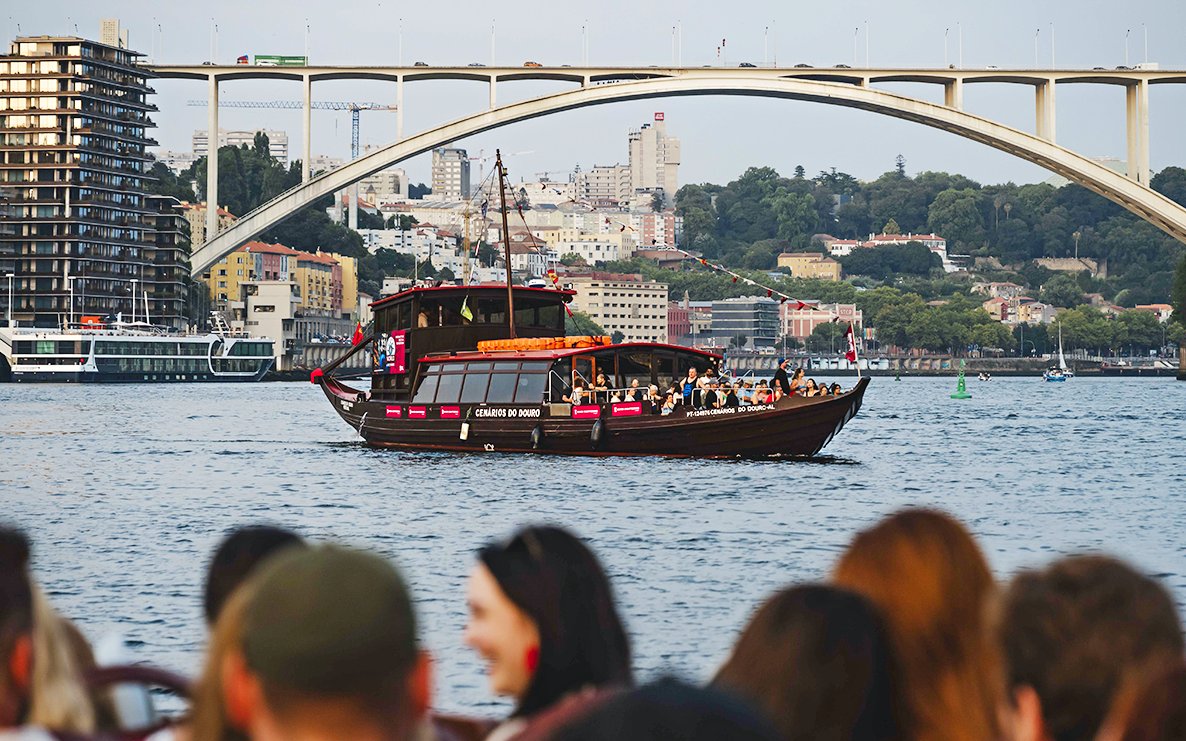 Tourists on a boat at Douro Pier with cityscape and bridge in the background.