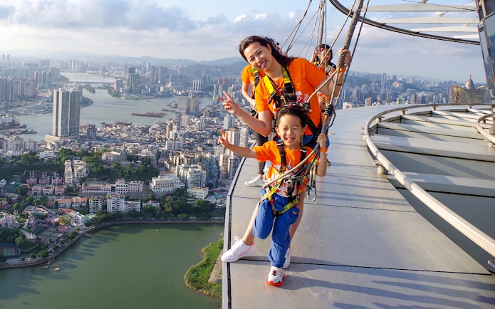 Visitors enjoying the Skywalk at Skypark Macau by AJ Hackett with cityscape view.