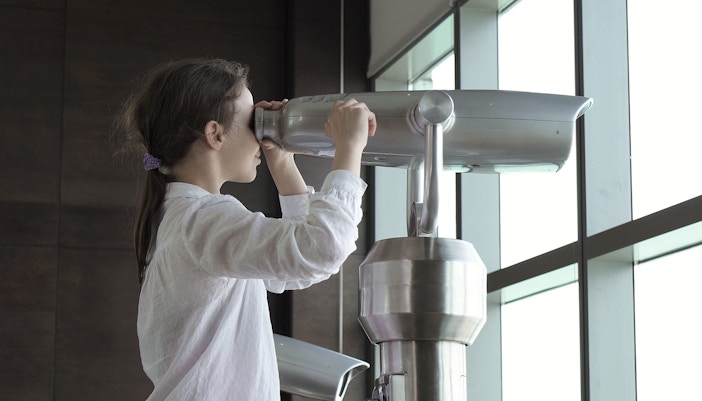 A teenage girl is looking through telescope from observation deck