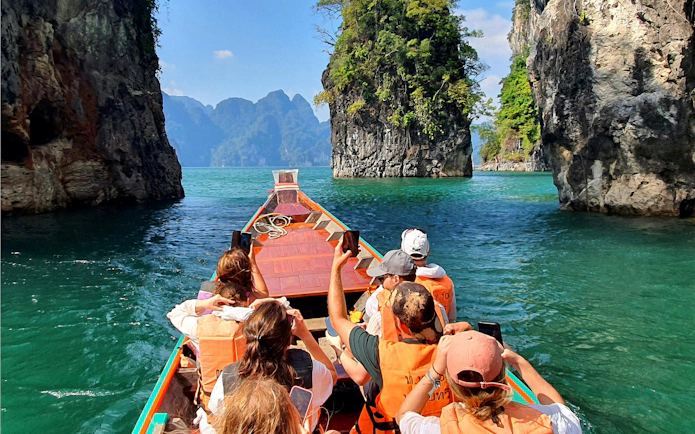 Boat tour on Cheow Lan Lake with tourists capturing limestone cliffs, Krabi, Thailand.