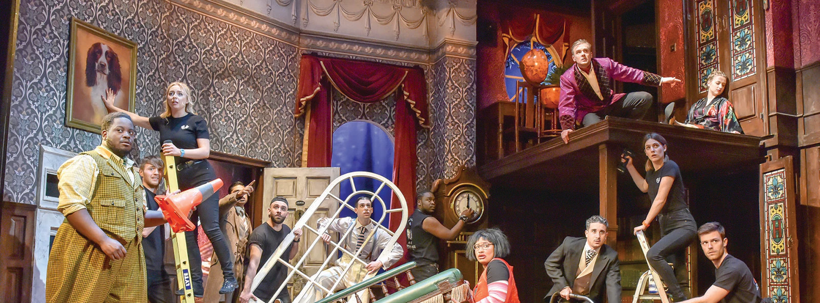 Cast performing a chaotic scene from "The Play That Goes Wrong" on stage.