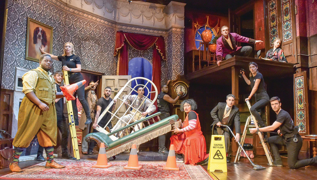 Cast performing a chaotic scene from "The Play That Goes Wrong" on stage.