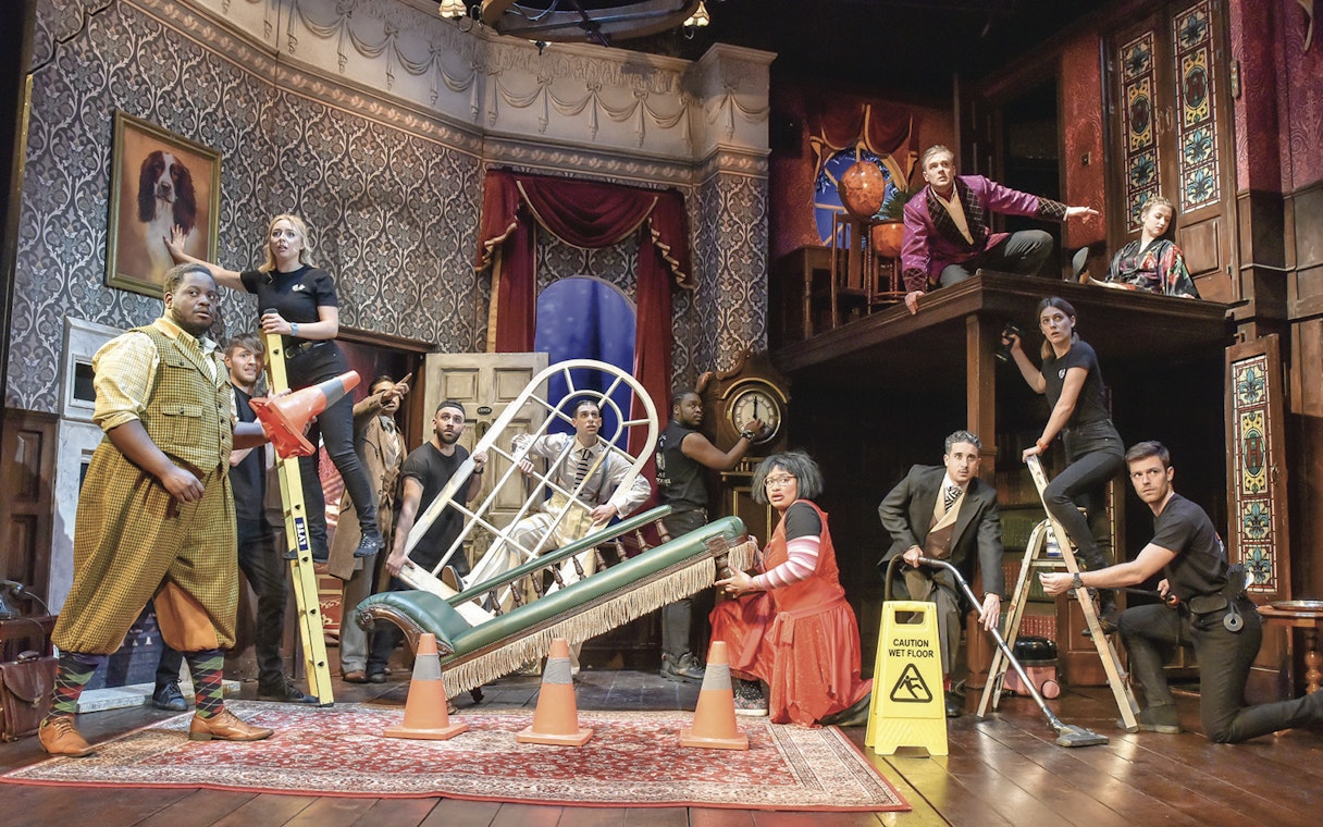 Cast performing a chaotic scene from "The Play That Goes Wrong" on stage.