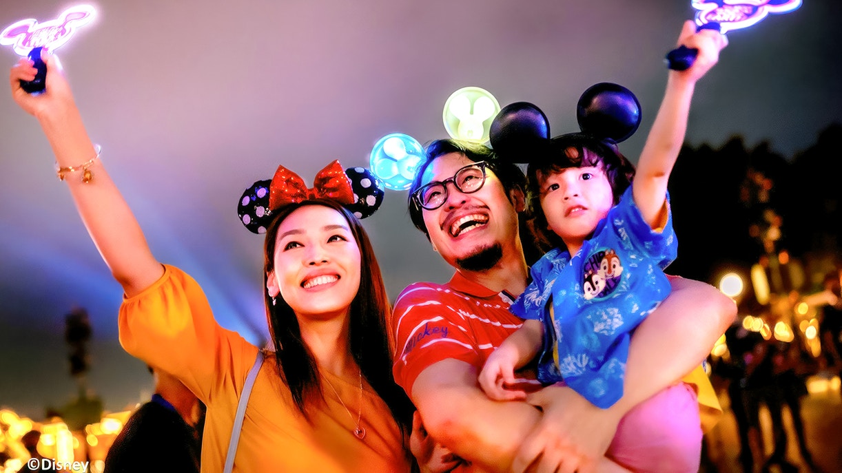 Family enjoying nighttime at Hong Kong Disneyland with Mickey Mouse ears.