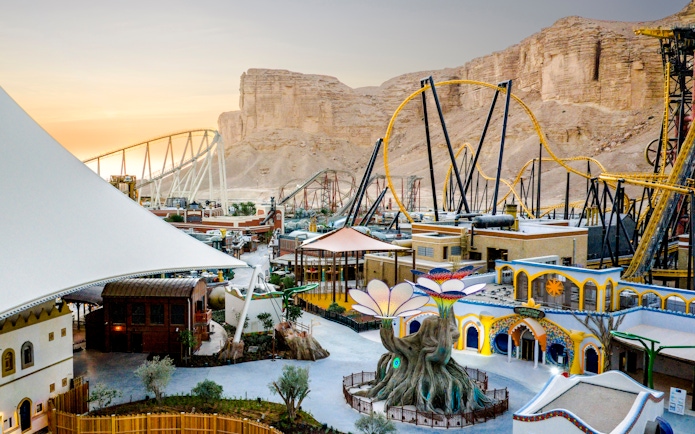 Aerial view of Six Flags Qiddiya with roller coasters and themed buildings against a desert backdrop.