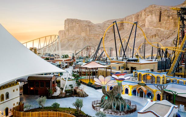 Aerial view of Six Flags Qiddiya with roller coasters and themed buildings against a desert backdrop.