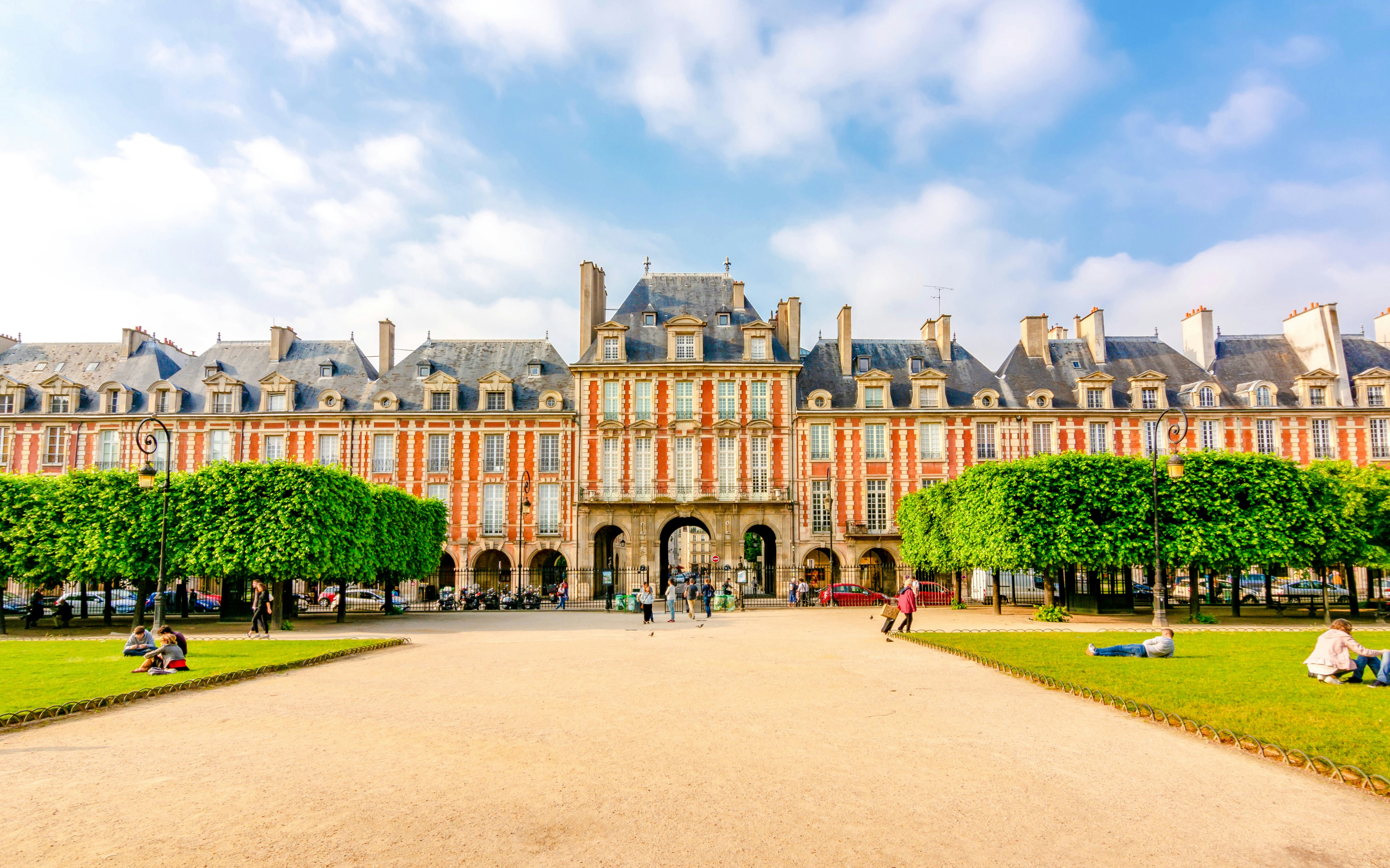 Place des Vosges in Paris with people relaxing on the grass and historic architecture in the background.