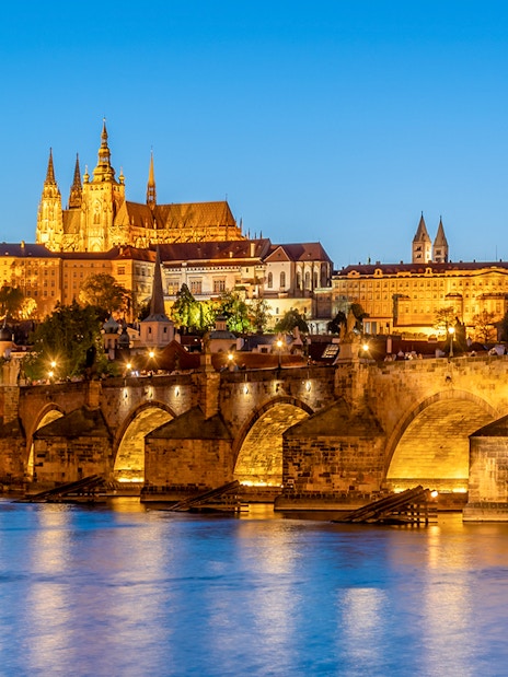 Prague Castle and Charles Bridge illuminated at night, view from Vltava River.