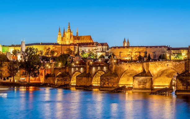 Prague Castle and Charles Bridge illuminated at night, view from Vltava River.