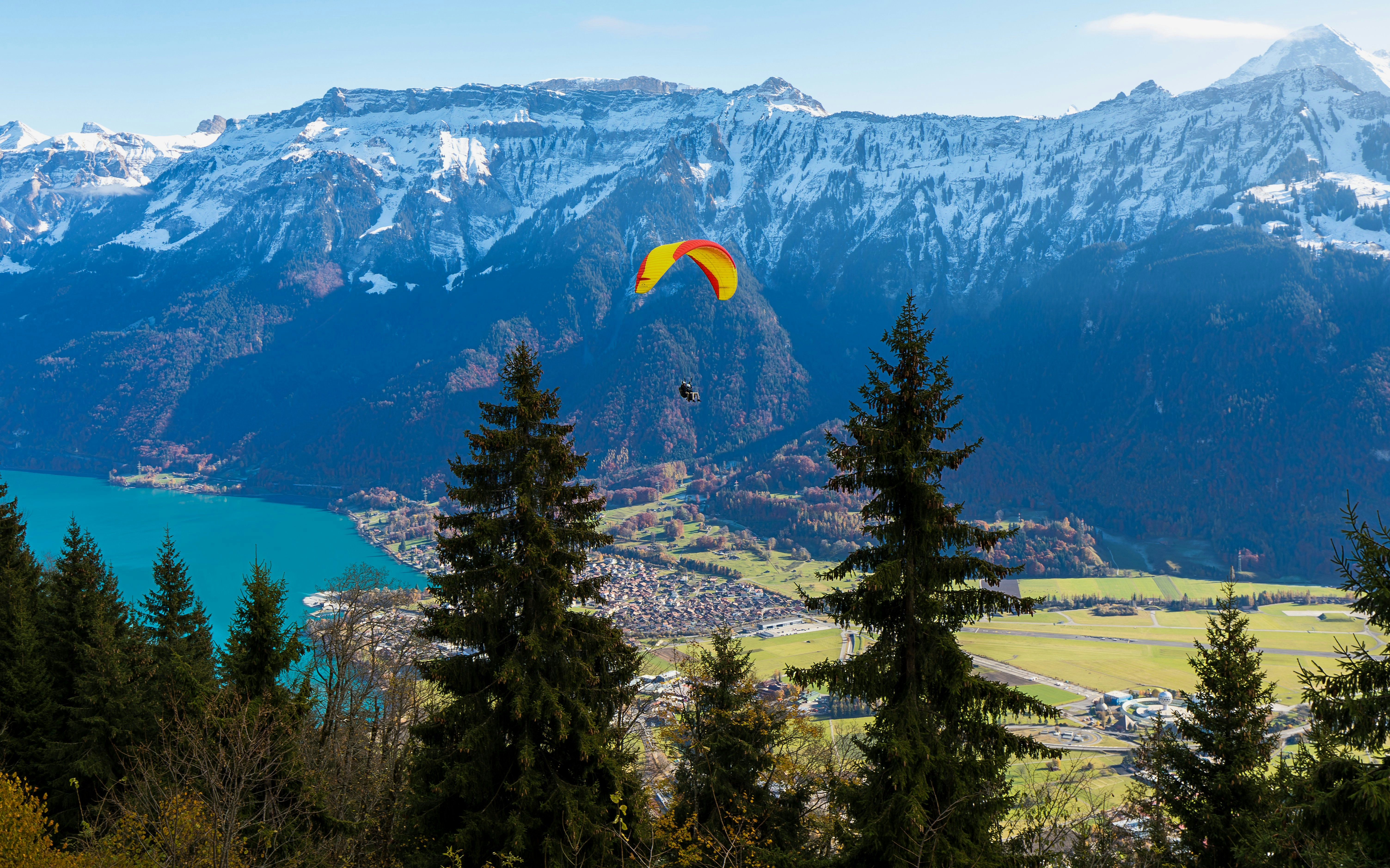 Paraglider soaring over Interlaken with Swiss Alps and Lake Thun in the background.