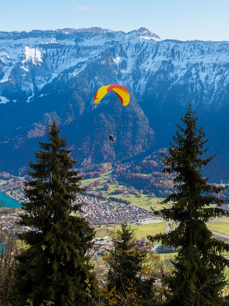 Paraglider soaring over Interlaken with Swiss Alps and Lake Thun in the background.