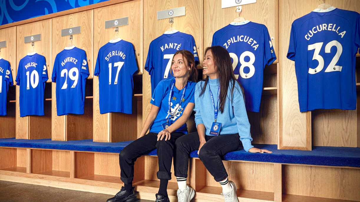Chelsea FC locker room with jerseys and visitors on a stadium tour.