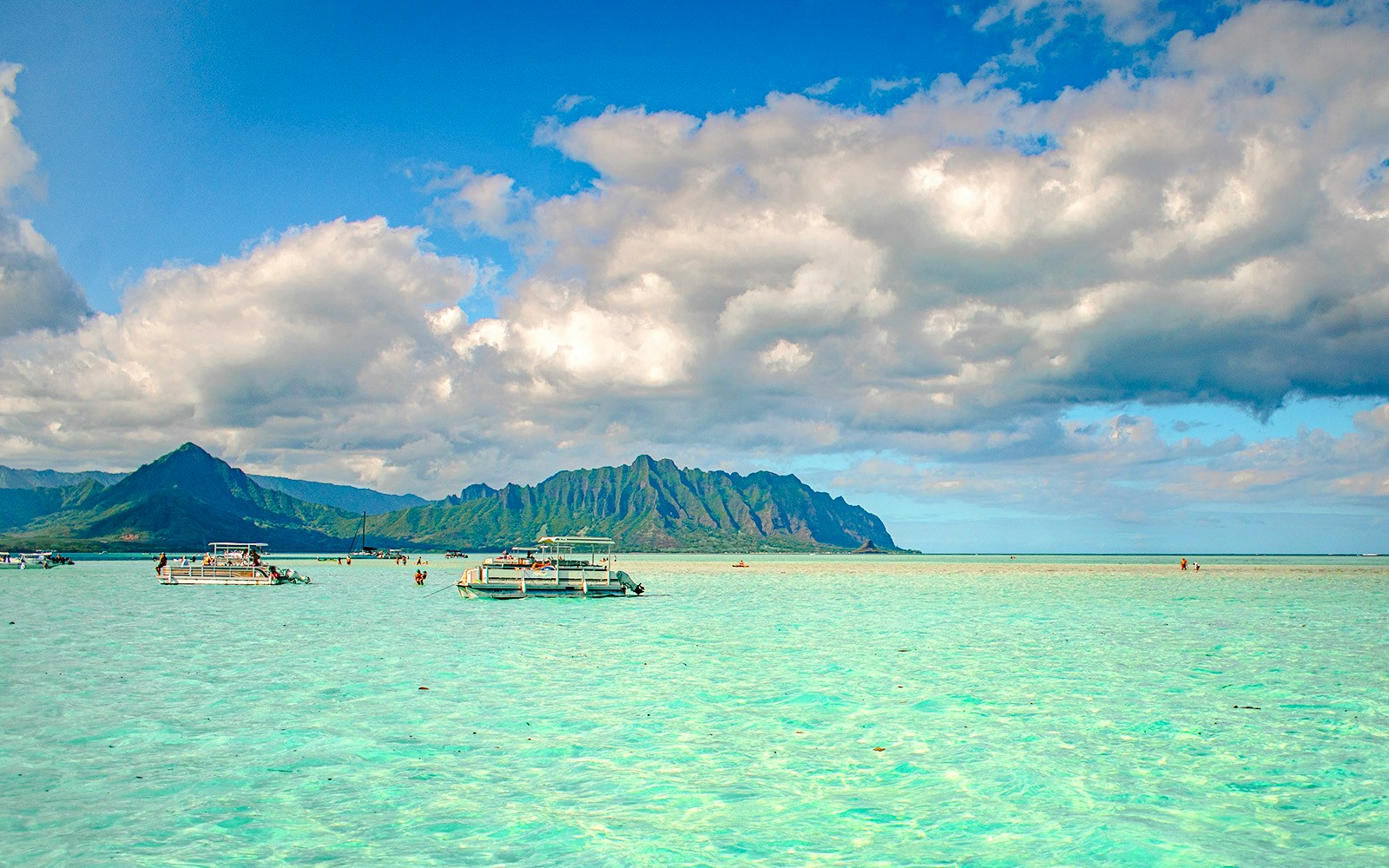 Boats on the turquoise waters of Kaneohe Bay with lush mountains in the background.