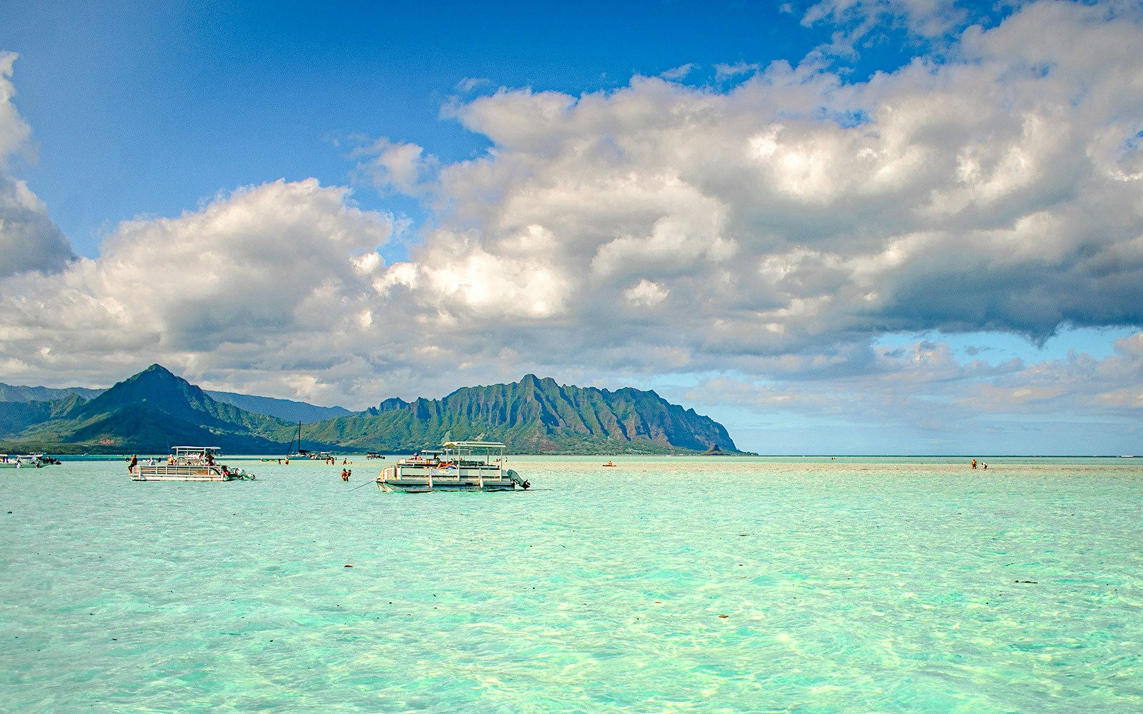 Boats on the turquoise waters of Kaneohe Bay with lush mountains in the background.