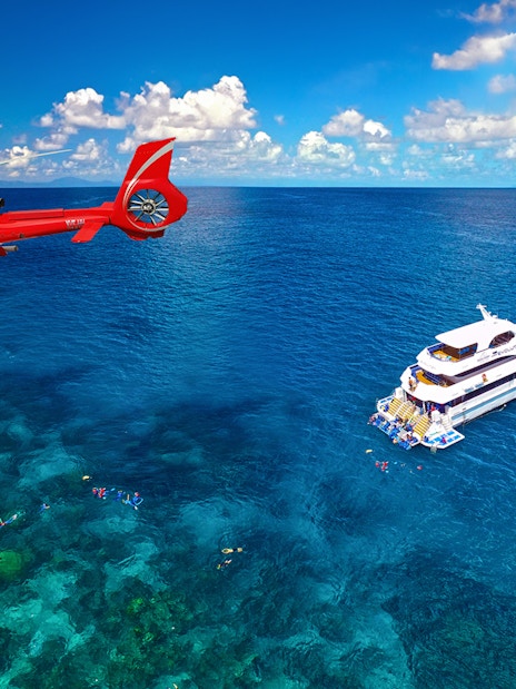Helicopter flying over Great Barrier Reef with cruise ship below.