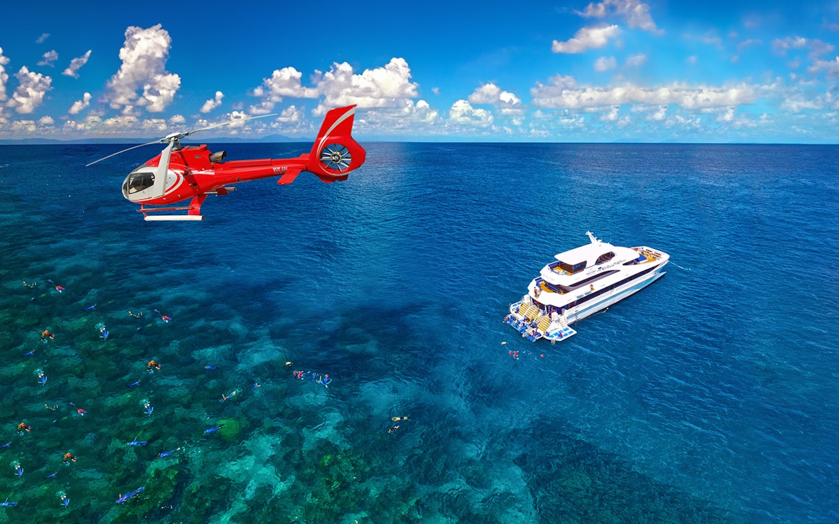 Helicopter flying over Great Barrier Reef with cruise ship below.