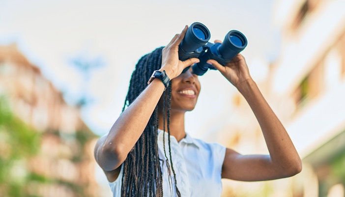 Tourist using binoculars to view distant landmarks in a scenic location.