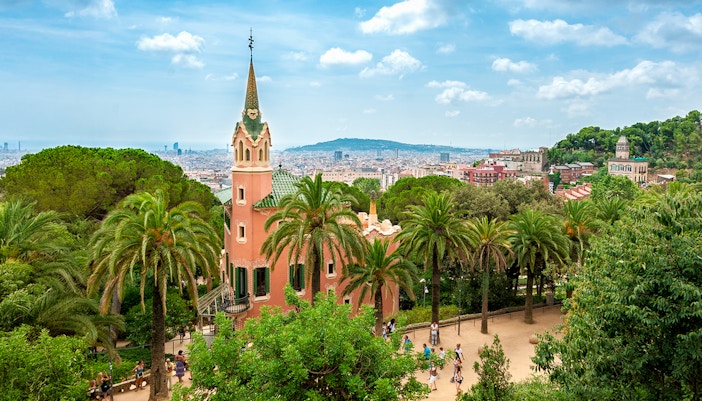 Gaudi House Museum in Park Güell, Barcelona, surrounded by palm trees and cityscape.