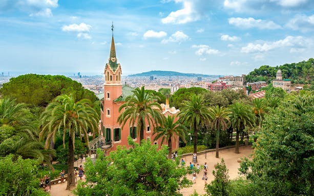 Gaudi House Museum in Park Güell, Barcelona, surrounded by palm trees and cityscape.