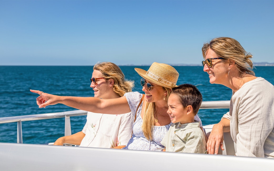 Tourists on cruise deck pointing at whale in ocean.