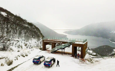 Off-road 4x4 vehicles at Mirador Paso Garibaldi with snowy view of Lakes Escondido and Fagnano.