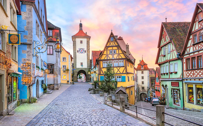 Cobblestone street in Rothenburg ob der Tauber with colorful half-timbered houses and medieval tower.