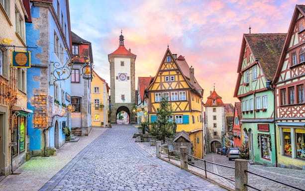 Cobblestone street in Rothenburg ob der Tauber with colorful half-timbered houses and medieval tower.