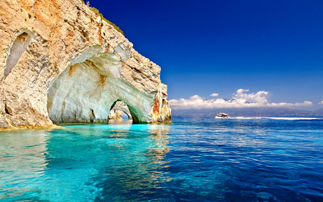Boat cruising near limestone arches on Zante coast, Greece.