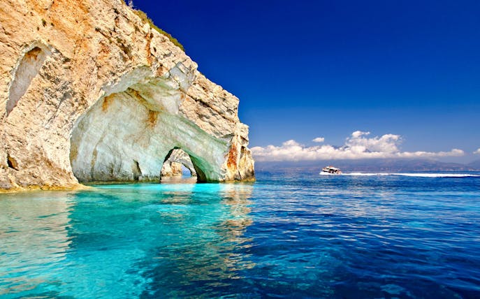 Boat cruising near limestone arches on Zante coast, Greece.