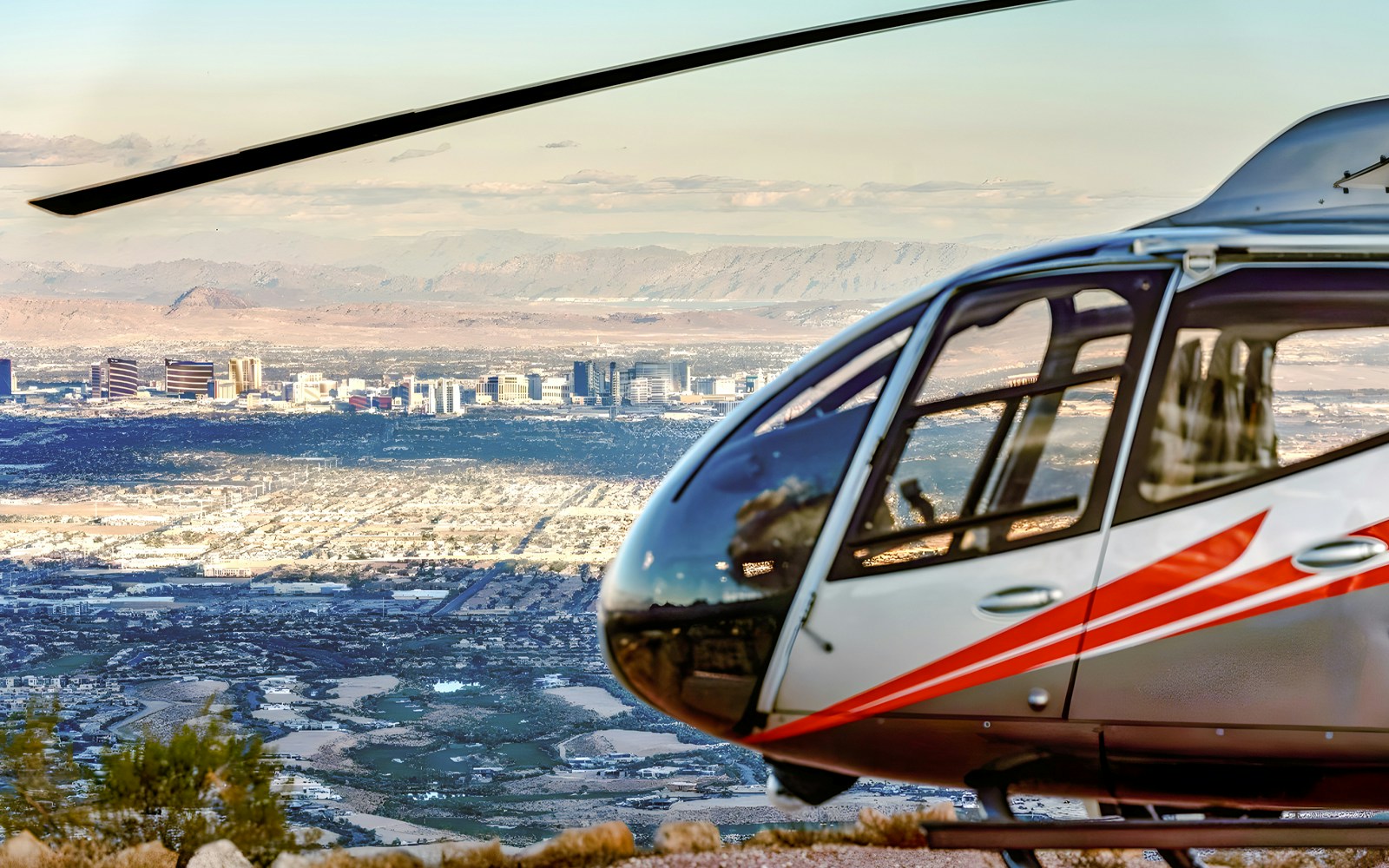 Silver and red Maverick helicopter over Las Vegas skyline with Red Rock Canyon in the background.