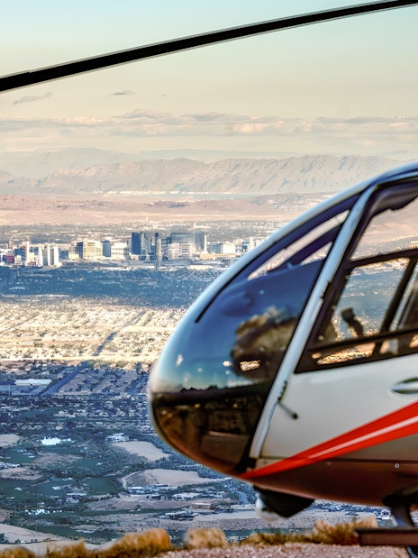 Silver and red Maverick helicopter with Las Vegas skyline and Red Rock Canyon in the background.