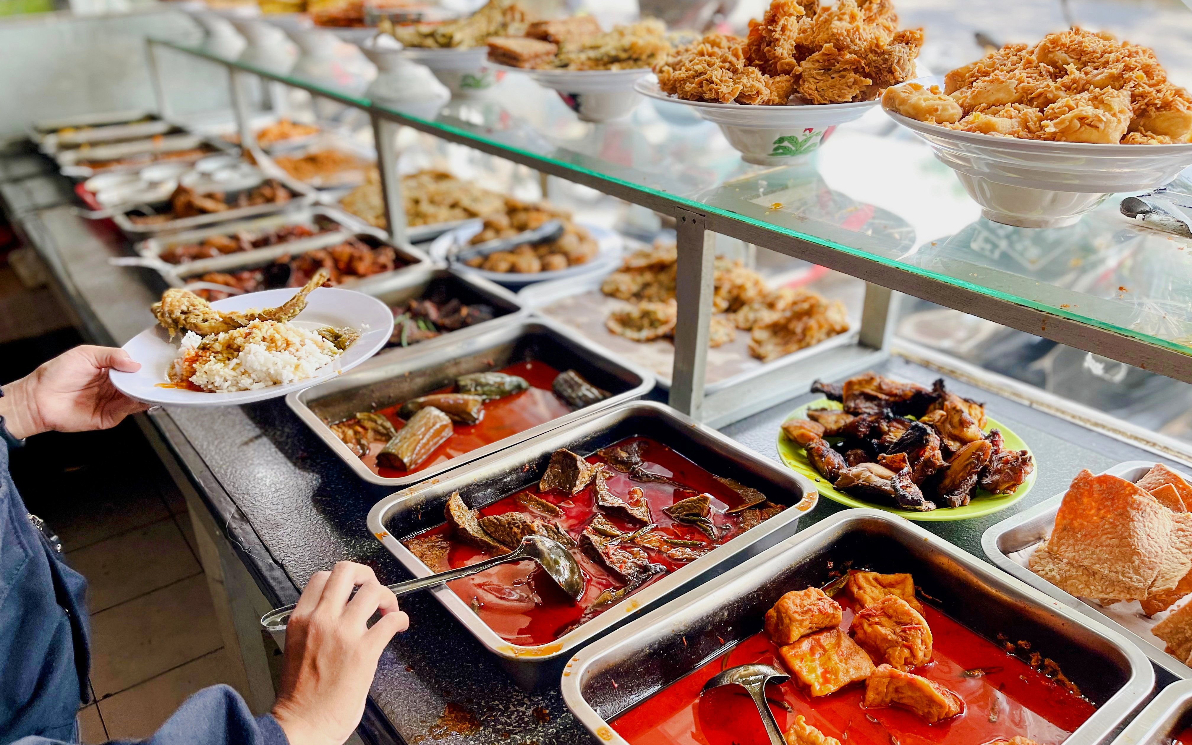 Padang food stall with various dishes and a person serving rice and fish.