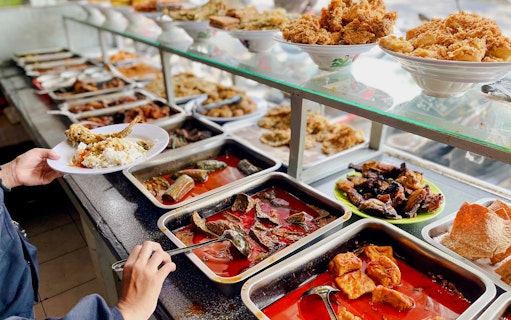 Padang food stall with various dishes and a person serving rice and fish.