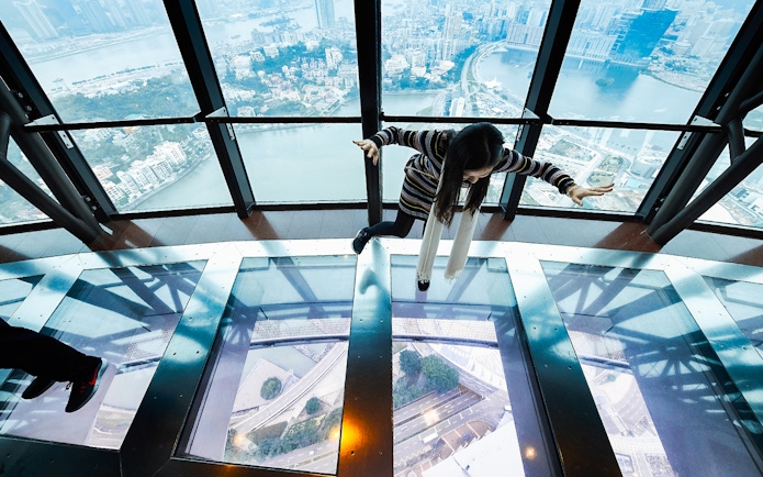 Person walking on glass floor at Macau Tower with city view below.