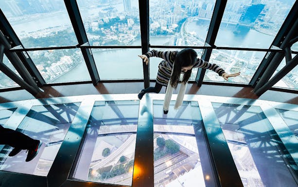 Person walking on glass floor at Macau Tower with city view below.