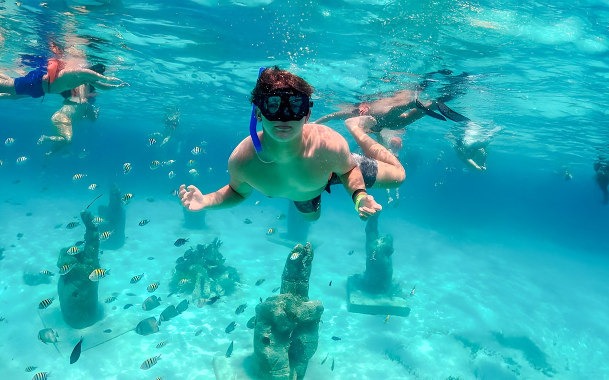 Snorkelers exploring underwater sculptures and fish in Isla Mujeres.