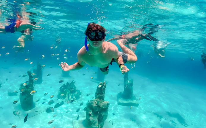 Snorkelers exploring underwater sculptures and fish in Isla Mujeres.