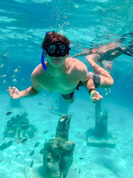 Snorkelers exploring underwater sculptures and fish in Isla Mujeres.