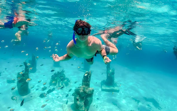 Snorkelers exploring underwater sculptures and fish in Isla Mujeres.