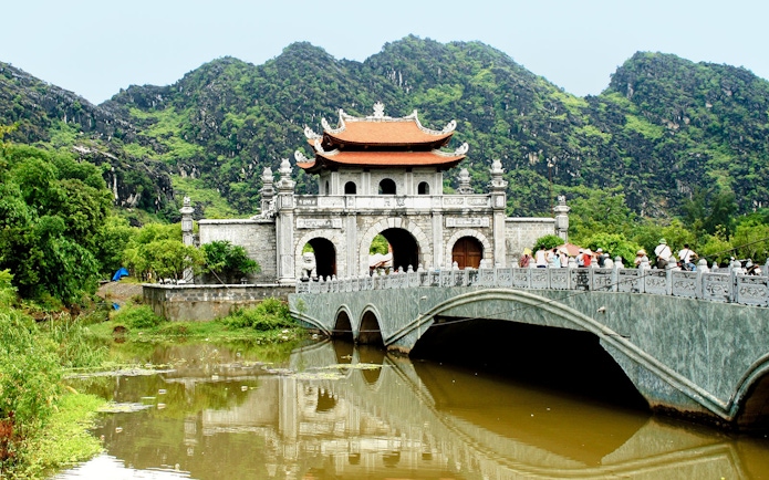 Hoa Lư Ancient Capital gate and bridge with lush mountains in Ninh Bình, Vietnam.