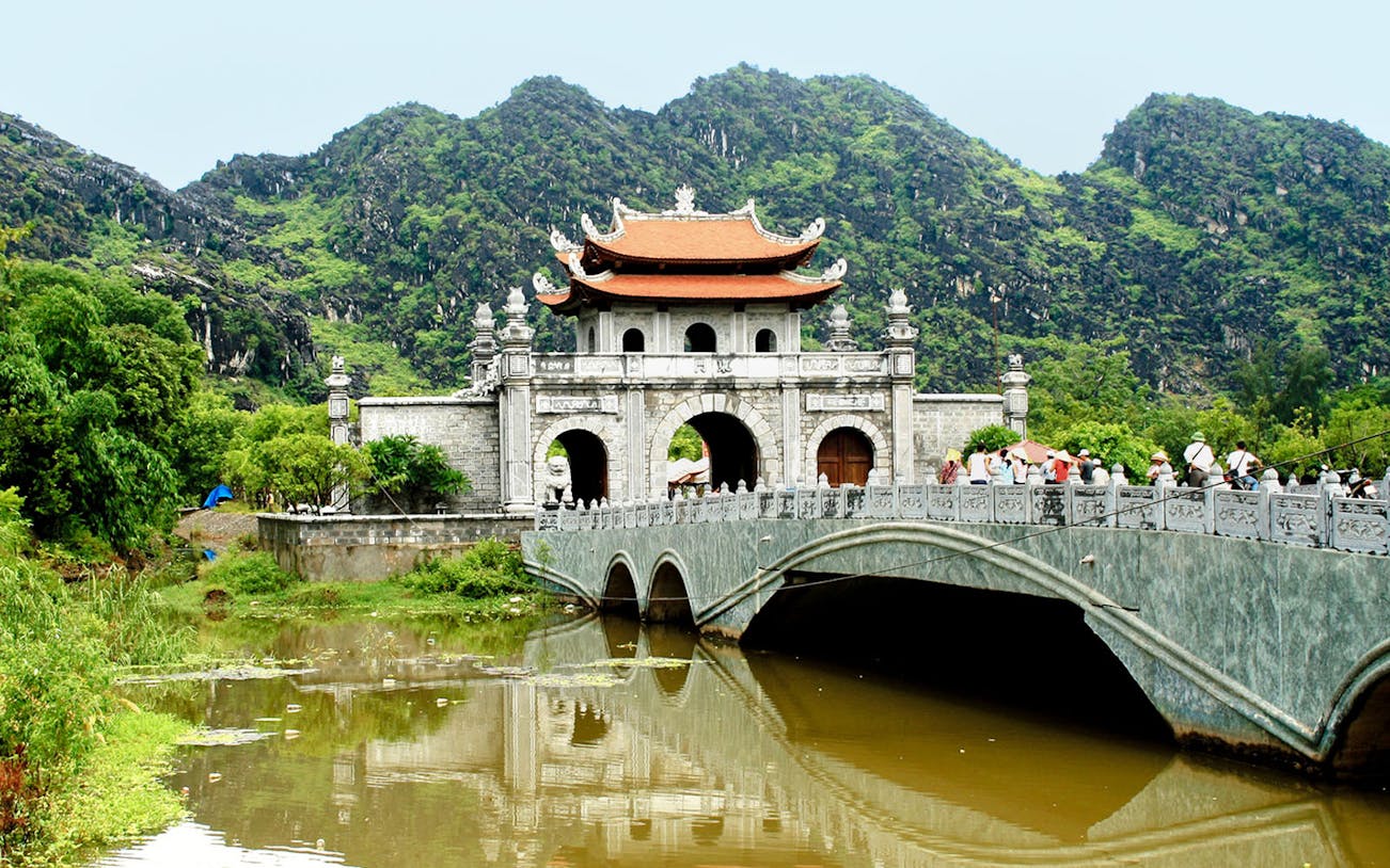 Hoa Lư Ancient Capital gate and bridge with lush mountains in Ninh Bình, Vietnam.