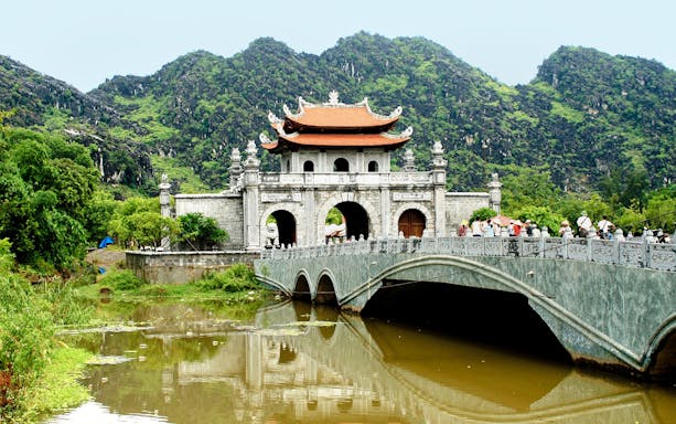 Hoa Lư Ancient Capital gate and bridge with lush mountains in Ninh Bình, Vietnam.