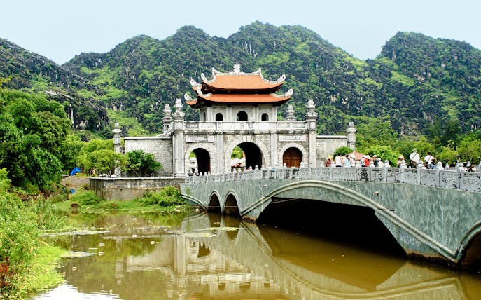 Hoa Lư Ancient Capital gate and bridge with lush mountains in Ninh Bình, Vietnam.