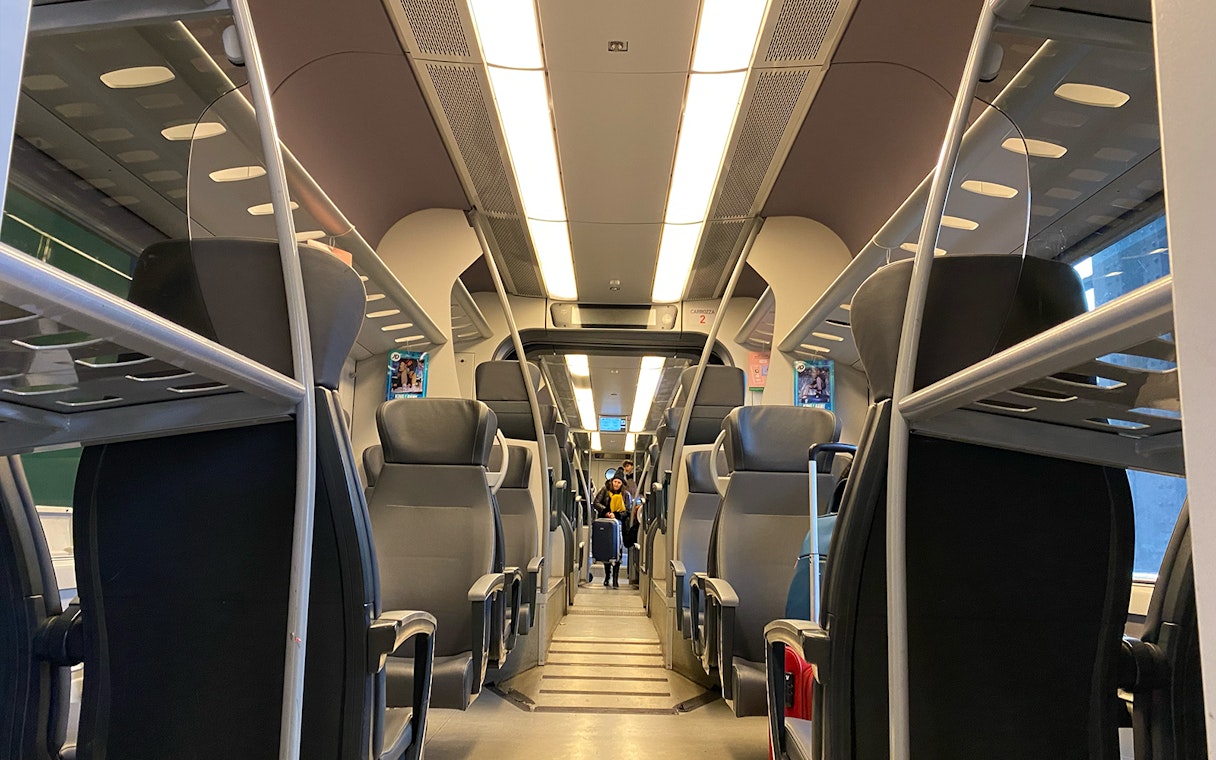 Interior view of Malpensa Express train with empty seats and overhead luggage racks.