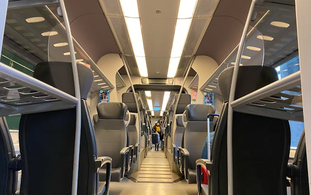 Interior view of Malpensa Express train with empty seats and overhead luggage racks.