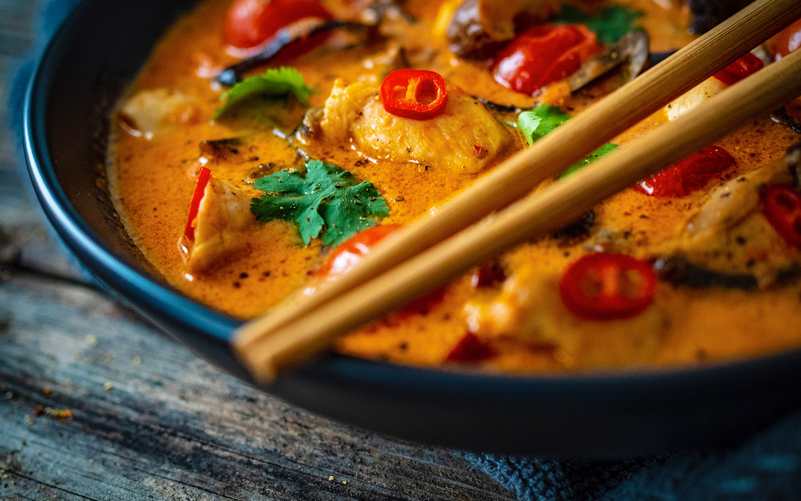 Thai red curry with chicken, red chilies, and cilantro in a bowl with chopsticks.