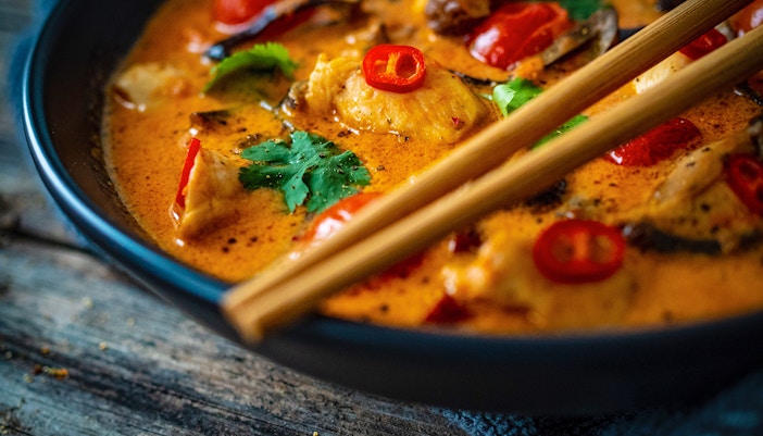 Thai red curry with chicken, red chilies, and cilantro in a bowl with chopsticks.