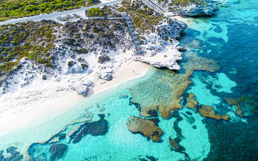 Aerial view of Rottnest Island's coastline with clear turquoise waters and rocky shoreline.