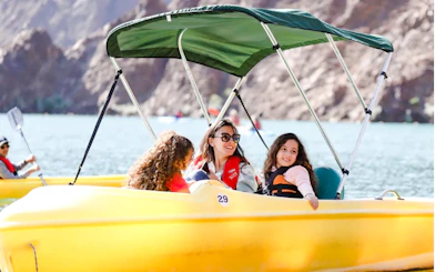 Family enjoying a pedal boat ride on Hatta Lake with mountain views, Sharjah.