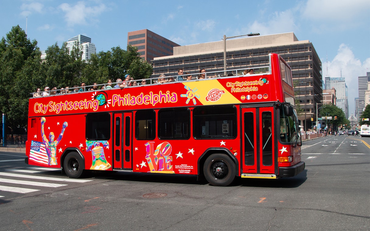 Red double-decker bus on Philadelphia Hop-On-Hop-Off Tour with city buildings in background.